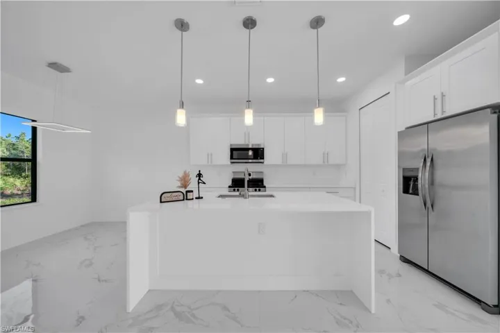 Kitchen featuring stainless steel appliances, light stone counters, white cabinetry, an island with sink, and light marble finish floors