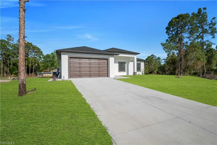 View of front of property featuring stucco siding, a front lawn, driveway, and a garage
