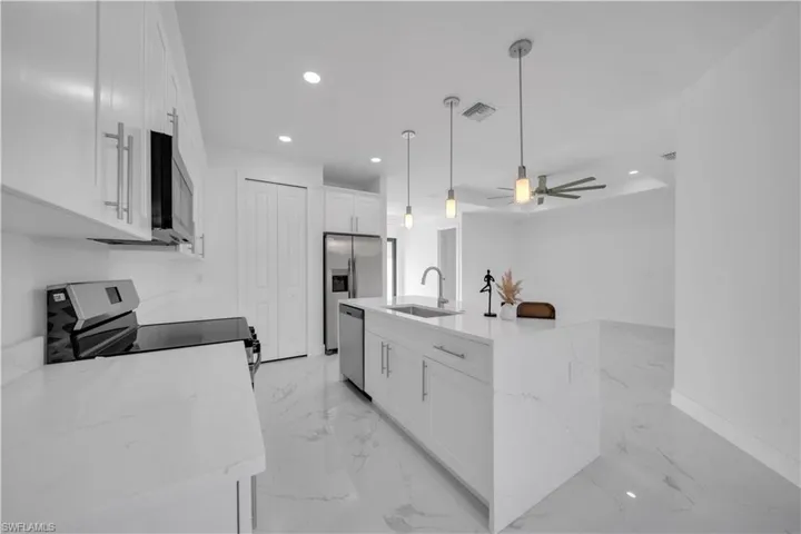 Kitchen with white cabinetry, light stone countertops, light marble finish flooring, stainless steel appliances, and a ceiling fan