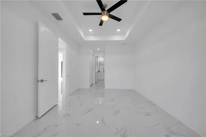 Empty room with recessed lighting, ceiling fan, light marble finish floors, and a raised ceiling