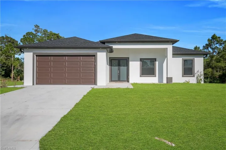 Prairie-style home featuring a front yard, stucco siding, an attached garage, and concrete driveway