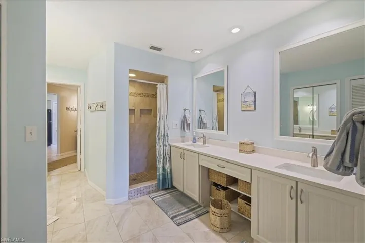 Full bath featuring double vanity, a tile shower, marble finish flooring, and recessed lighting