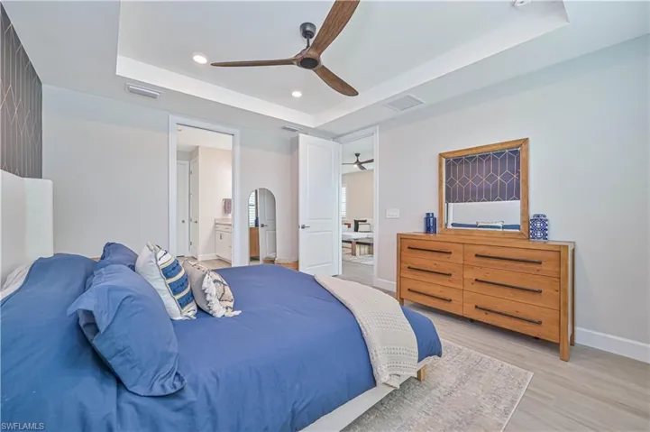 Bedroom with ceiling fan, connected bathroom, a tray ceiling, and light hardwood / wood-style flooring