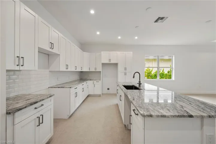 Kitchen with white cabinetry, light stone counters, recessed lighting, an island with sink, and backsplash