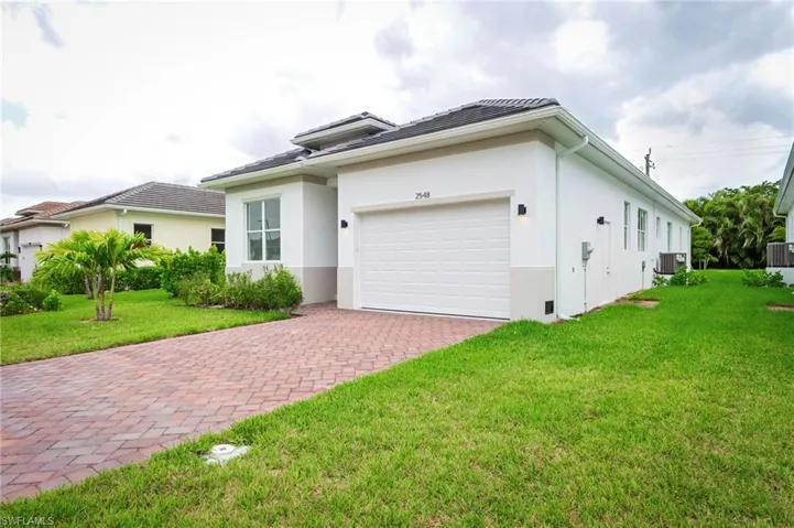 View of front facade featuring a front lawn, stucco siding, decorative driveway, a garage, and a tile roof