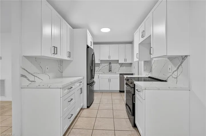 Kitchen featuring light stone counters, appliances with stainless steel finishes, light tile patterned floors, and white cabinetry