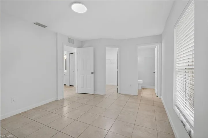 Unfurnished bedroom with connected bathroom, light tile patterned floors, and a spacious closet