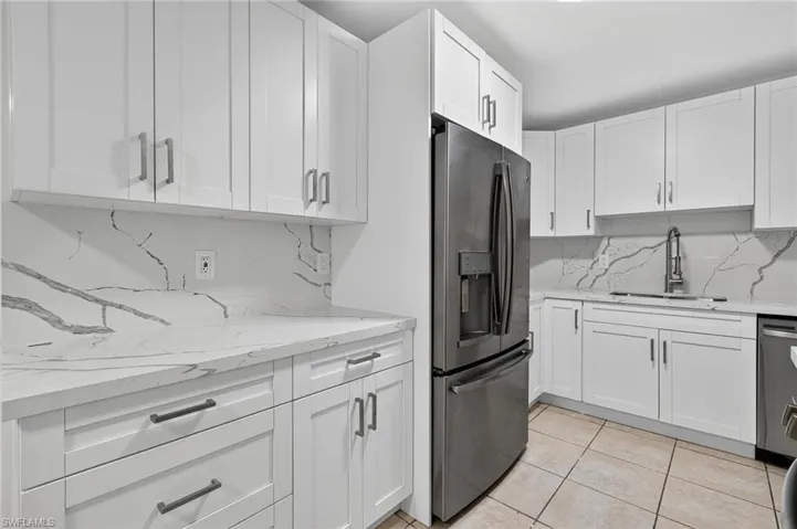 Kitchen featuring backsplash, white cabinetry, appliances with stainless steel finishes, light tile patterned floors, and light stone countertops