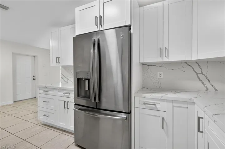 Kitchen featuring stainless steel fridge, light stone countertops, backsplash, white cabinetry, and light tile patterned floors