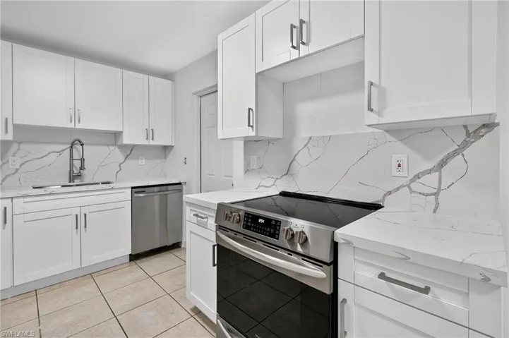 Kitchen featuring appliances with stainless steel finishes, white cabinetry, light stone counters, and light tile patterned floors