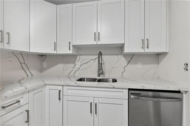 Kitchen featuring white cabinets, light stone counters, dishwasher, and decorative backsplash