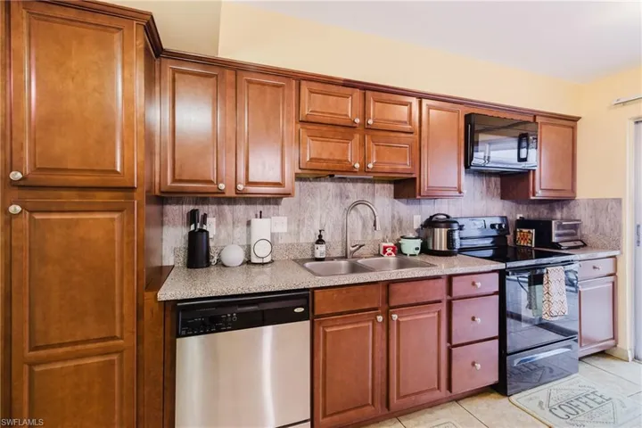 Kitchen with black appliances, a sink, light tile patterned flooring, light countertops, and decorative backsplash