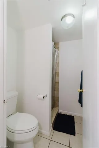 Full bathroom with tile patterned floors, tiled shower, toilet, and baseboards