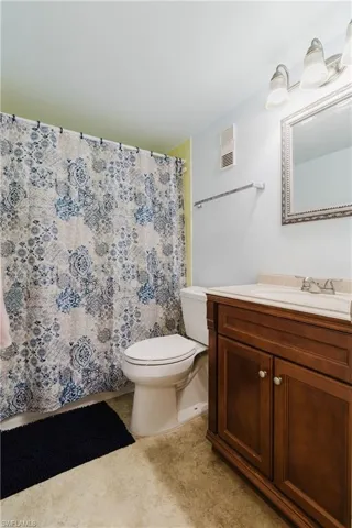 Full bathroom featuring vanity, a shower with shower curtain, visible vents, tile patterned floors, and toilet