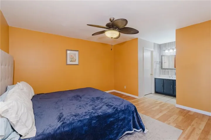 Bedroom featuring ensuite bath, light wood-type flooring, baseboards, and a ceiling fan
