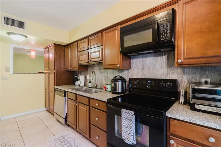 Kitchen featuring visible vents, decorative backsplash, brown cabinetry, black appliances, and a sink