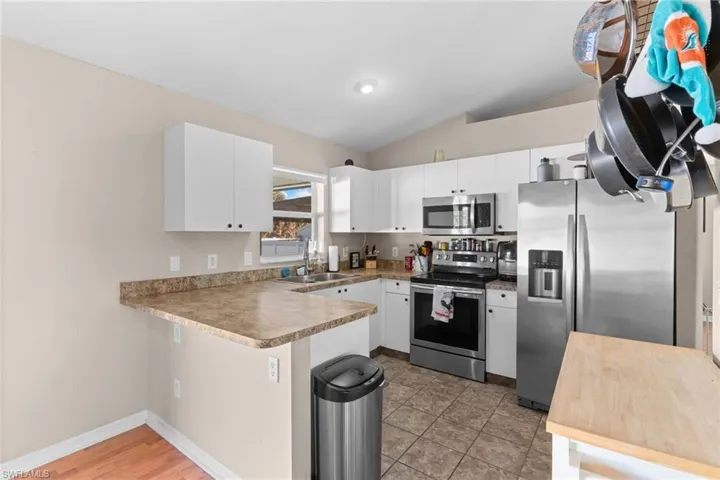 Kitchen featuring stainless steel appliances, a peninsula, lofted ceiling, light countertops, and white cabinetry