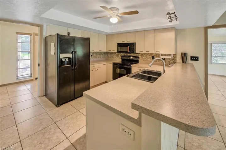 Kitchen with sink, black appliances, kitchen peninsula, a raised ceiling, and cream cabinetry