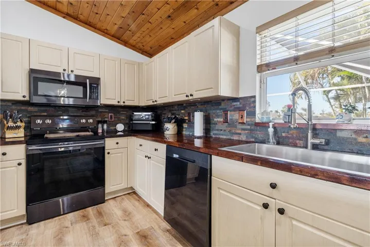Kitchen with black appliances, dark countertops, tasteful backsplash, light wood-style flooring, and a vaulted wooden ceiling