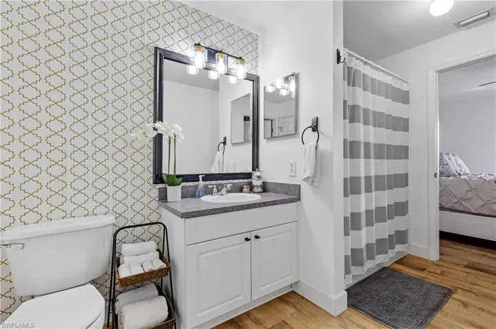 Ensuite bathroom with vanity, a shower with curtain, light wood-style floors, and wallpapered walls