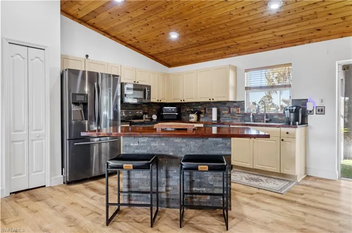 Kitchen with stainless steel appliances, a vaulted wooden ceiling, a kitchen breakfast bar, a center island, and tasteful backsplash