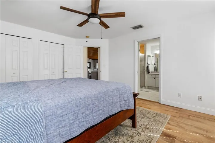 Bedroom with multiple closets, wood finished floors, a ceiling fan, and ensuite bath