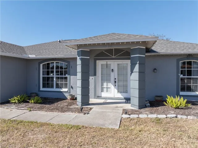 Doorway to property featuring a shingled roof, stucco siding, a lawn, and french doors