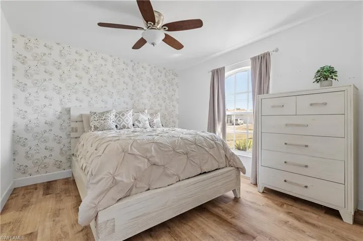 Bedroom with light wood-type flooring, a ceiling fan, and wallpapered walls
