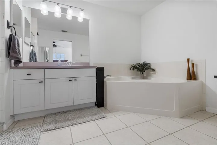Bathroom featuring vanity, a bath, light tile patterned floors, ceiling fan, and tile walls