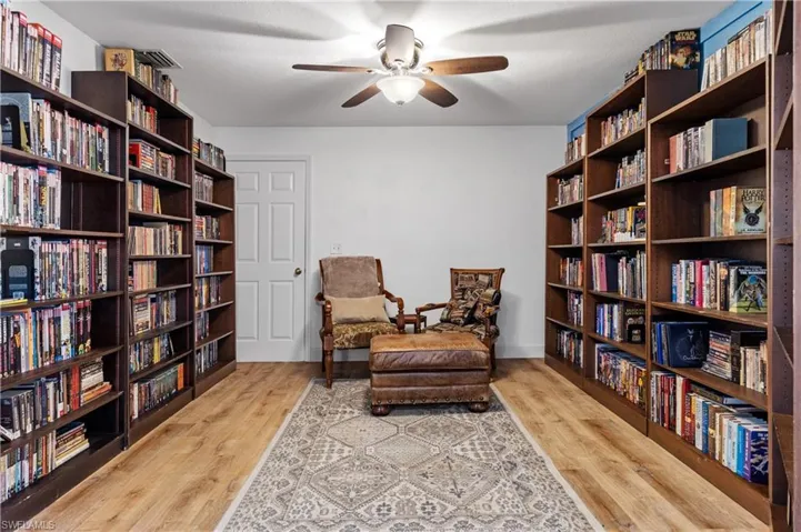Sitting room with bookshelves, ceiling fan, and light wood finished floors