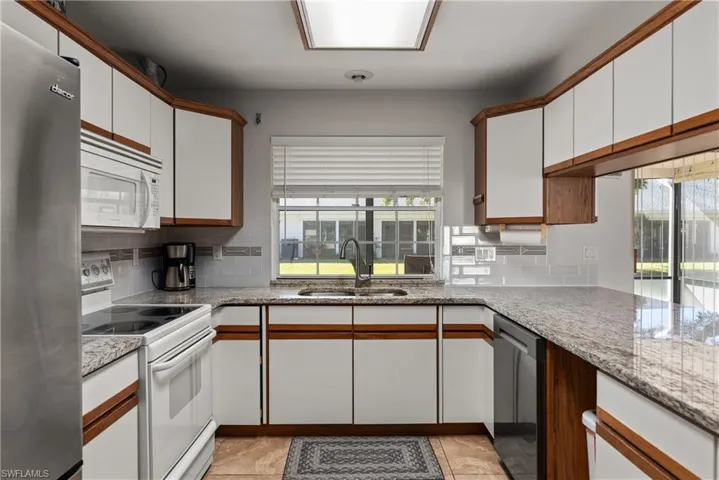 Kitchen featuring appliances with stainless steel finishes, white cabinets, brown cabinets, light tile patterned floors, and light stone counters