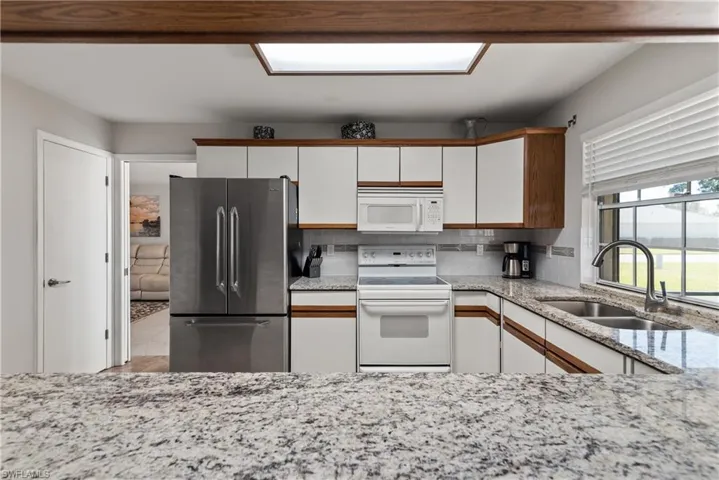 Kitchen with white appliances, white cabinetry, light stone countertops, decorative backsplash, and brown cabinets