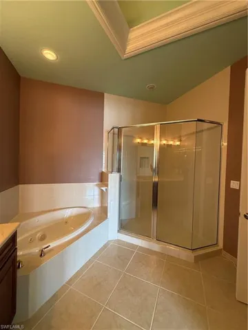 Full bath featuring a stall shower, vanity, light tile patterned floors, a jetted tub, and ornamental molding