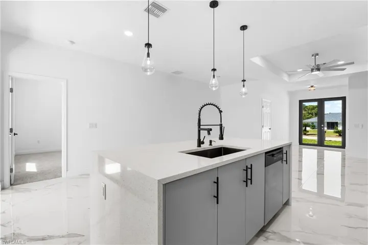Kitchen with an island with sink, gray cabinetry, light stone counters, a tray ceiling, and a ceiling fan