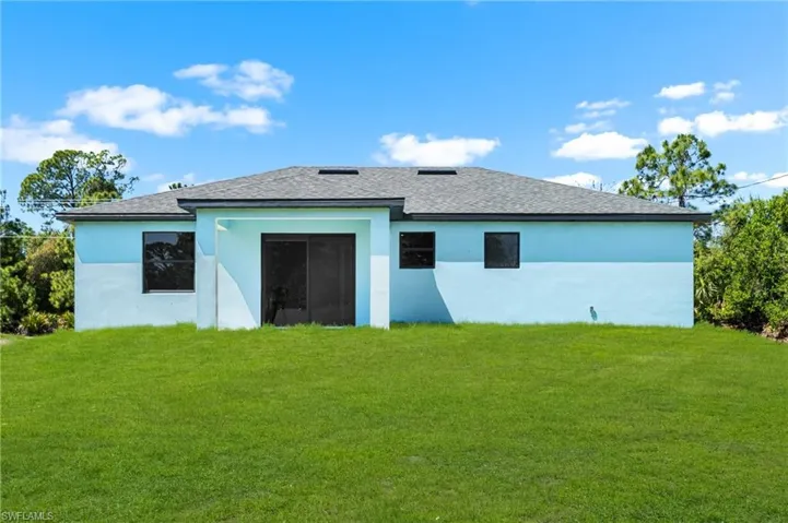 Back of house with a yard, stucco siding, and a shingled roof