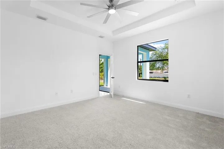 Carpeted spare room featuring a tray ceiling and ceiling fan