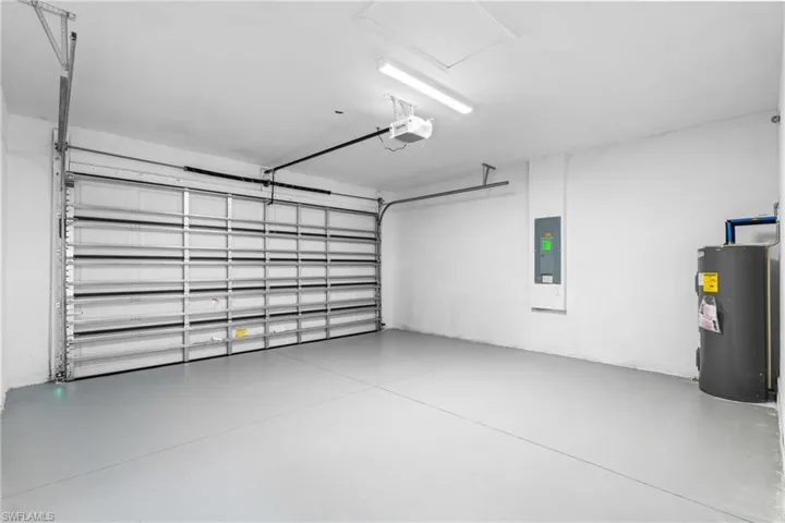 Garage featuring electric water heater, electric panel, and a garage door opener