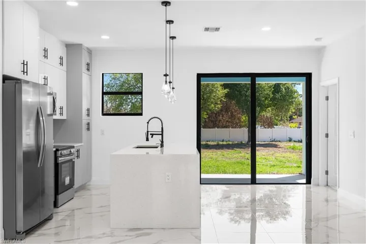 Kitchen featuring stainless steel appliances, decorative light fixtures, white cabinets, light stone countertops, and light marble finish floors