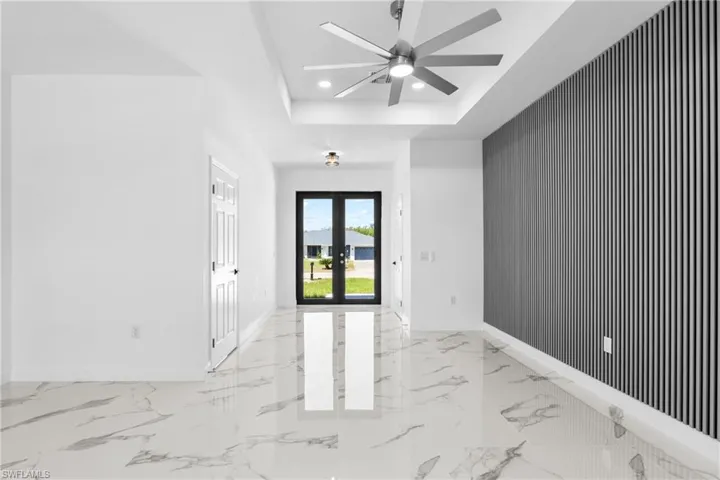 Empty room with french doors, an accent wall, recessed lighting, ceiling fan, and light marble finish flooring