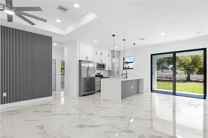 Kitchen featuring stainless steel appliances, a center island with sink, light marble finish floors, white cabinetry, and light stone countertops