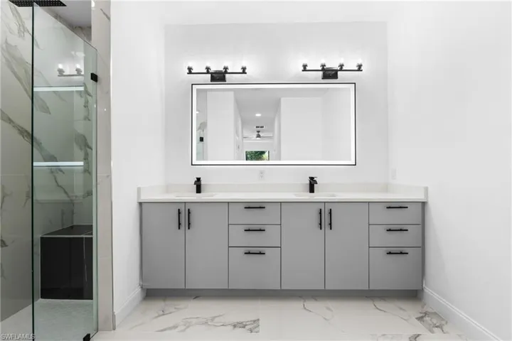 Bathroom featuring double vanity, a marble finish shower, and light marble finish floors