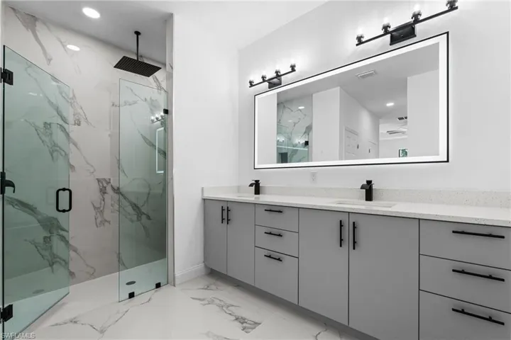 Full bathroom with double vanity, a marble finish shower, recessed lighting, and light marble finish floors