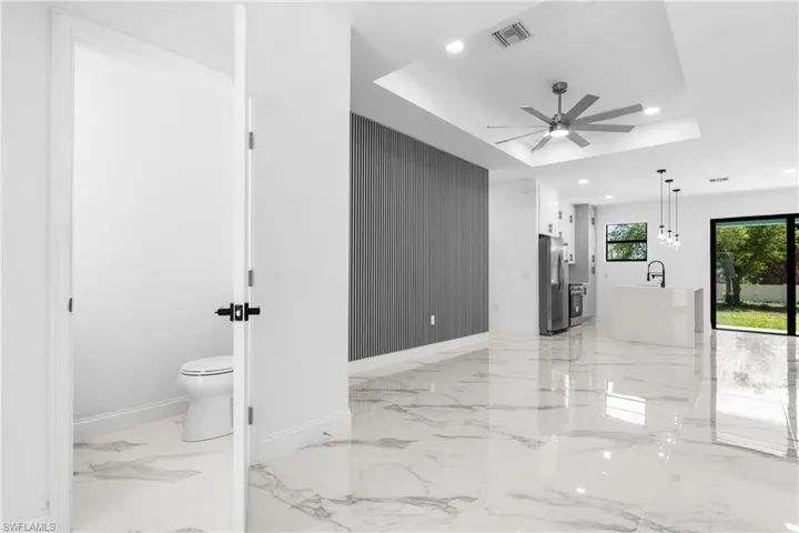 Living area featuring a raised ceiling, a ceiling fan, recessed lighting, and light marble finish flooring