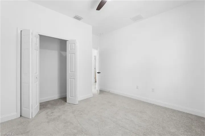 Unfurnished bedroom featuring light colored carpet, a closet, and a ceiling fan
