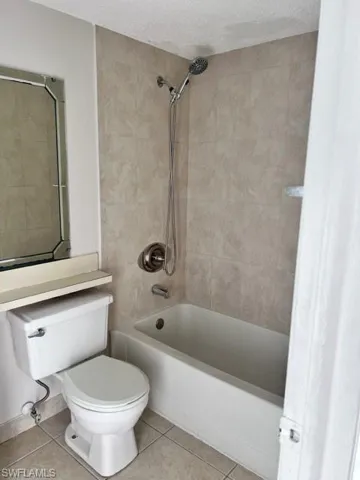 Full bath with light tile patterned floors, shower / washtub combination, and a textured ceiling