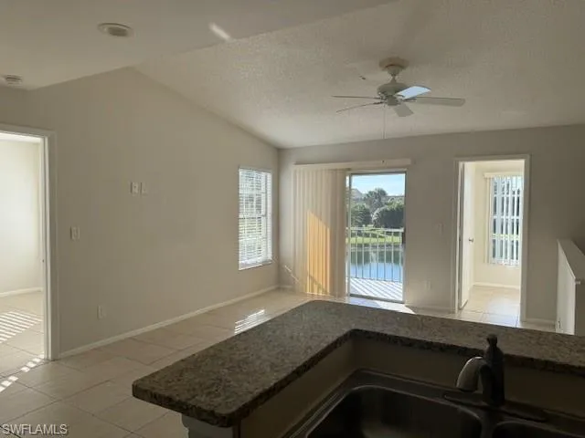 Kitchen featuring light tile patterned flooring, a textured ceiling, a water view, ceiling fan, and lofted ceiling