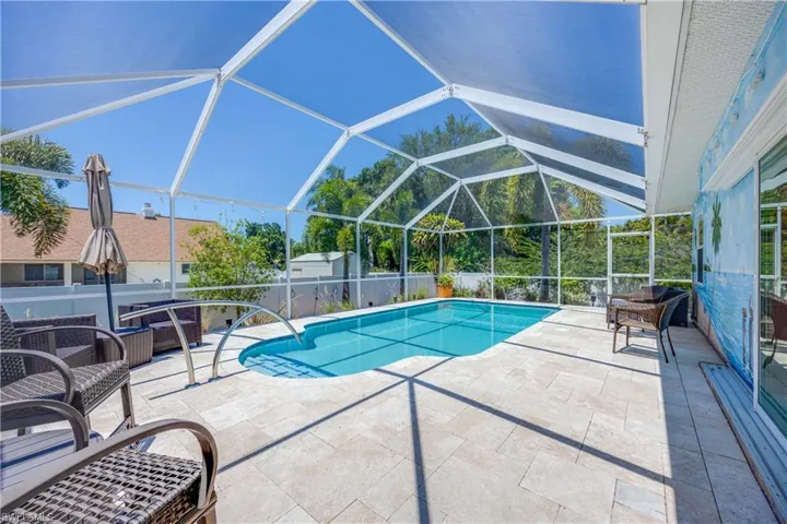 View of heated swimming pool with large screened in lanai and travertine pavers