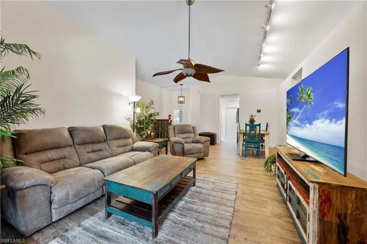 Living room featuring vaulted ceiling, track lighting, ceiling fan, and wood like tile flooring