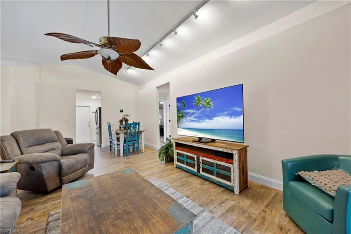 Living room featuring wood-style tile flooring, track lighting, lofted ceiling, and ceiling fan