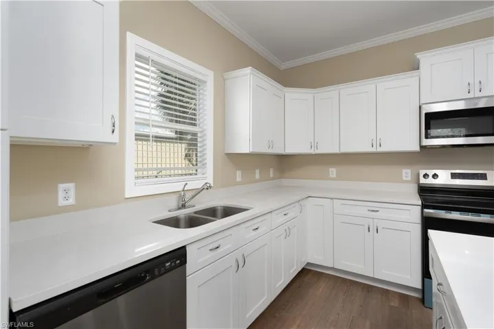 Kitchen featuring stainless steel appliances, white cabinets, ornamental molding, dark wood-style floors, and light stone counters